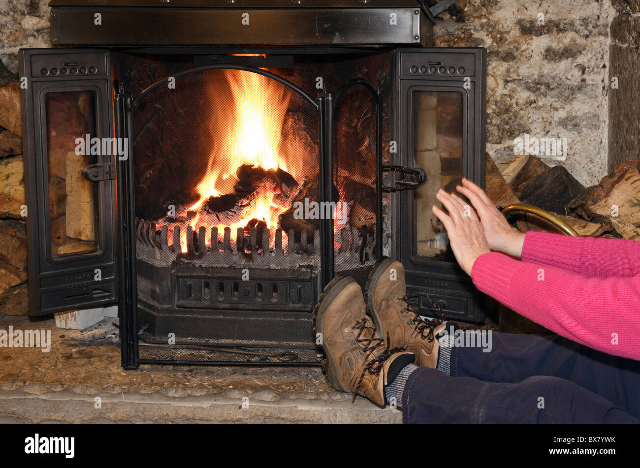 England, UK. Person trägt Stiefel Erwärmung kalte Hände und Füße saßen vor einem offenen Kamin zu Hause Stockfoto