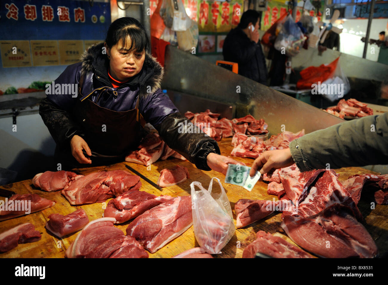 Ein Schwein-Anbieter nimmt Renminbi Banknoten von einem Kunden auf einem Markt in Peking, China. 1. Dezember 2010 Stockfoto