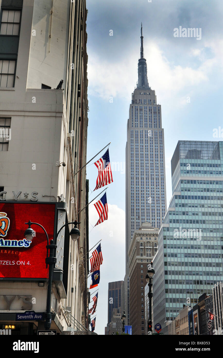 Amerikanische Flaggen wehen außerhalb Macy Store an der Seventh Avenue mit dem Empire State Building im Hintergrund Stockfoto