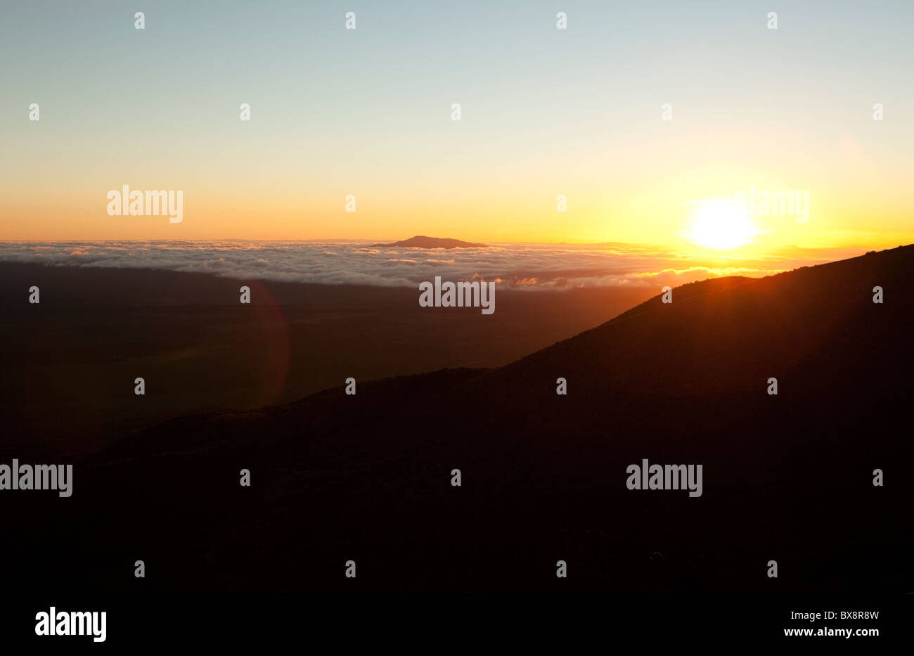 Sonnenuntergang am Vulkan Mauna Kea in Hawaii mit Wolken unter und untergehende Sonne mit Bergen silhouette Stockfoto