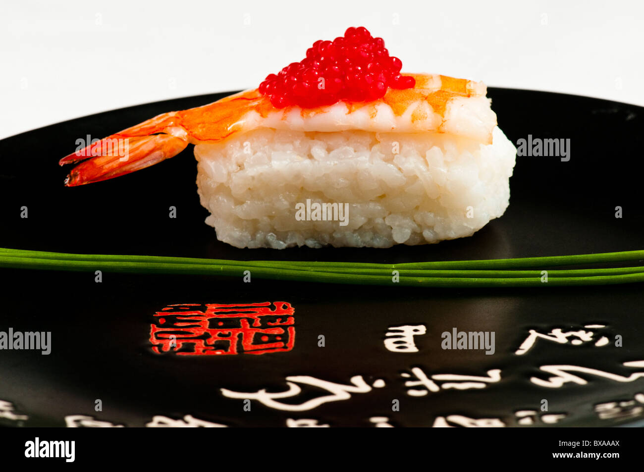 Nigiri Sushi mit Garnele, roter Fisch, Eiern und garniert mit Schnittlauch.  Auf einer schwarzen Platte mit dem japanischen schreiben in rot und weiß. Stockfoto