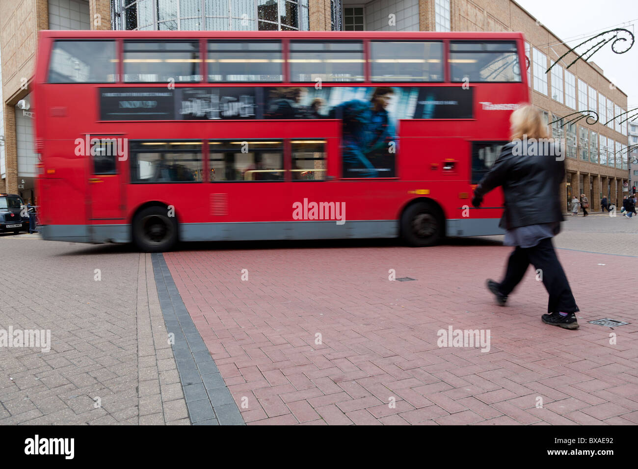 Eine Frau kreuzen die Straße als Doppeldeckerbus vorbei, Kingston, Surrey, England. Stockfoto