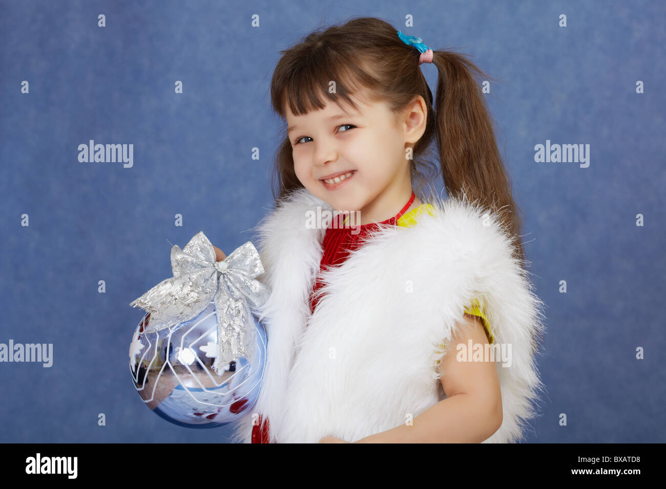 Das kleine Mädchen in einem weißen Pelz Kostüm hält eine Glaskugel auf blau Stockfoto