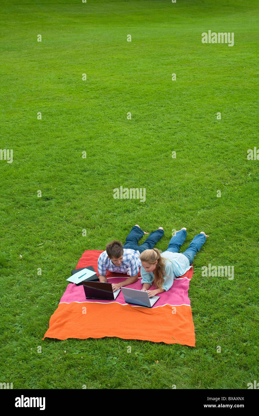 Mitte erwachsenes paar auf Rasen im Park liegen und mit Notebooks Stockfoto