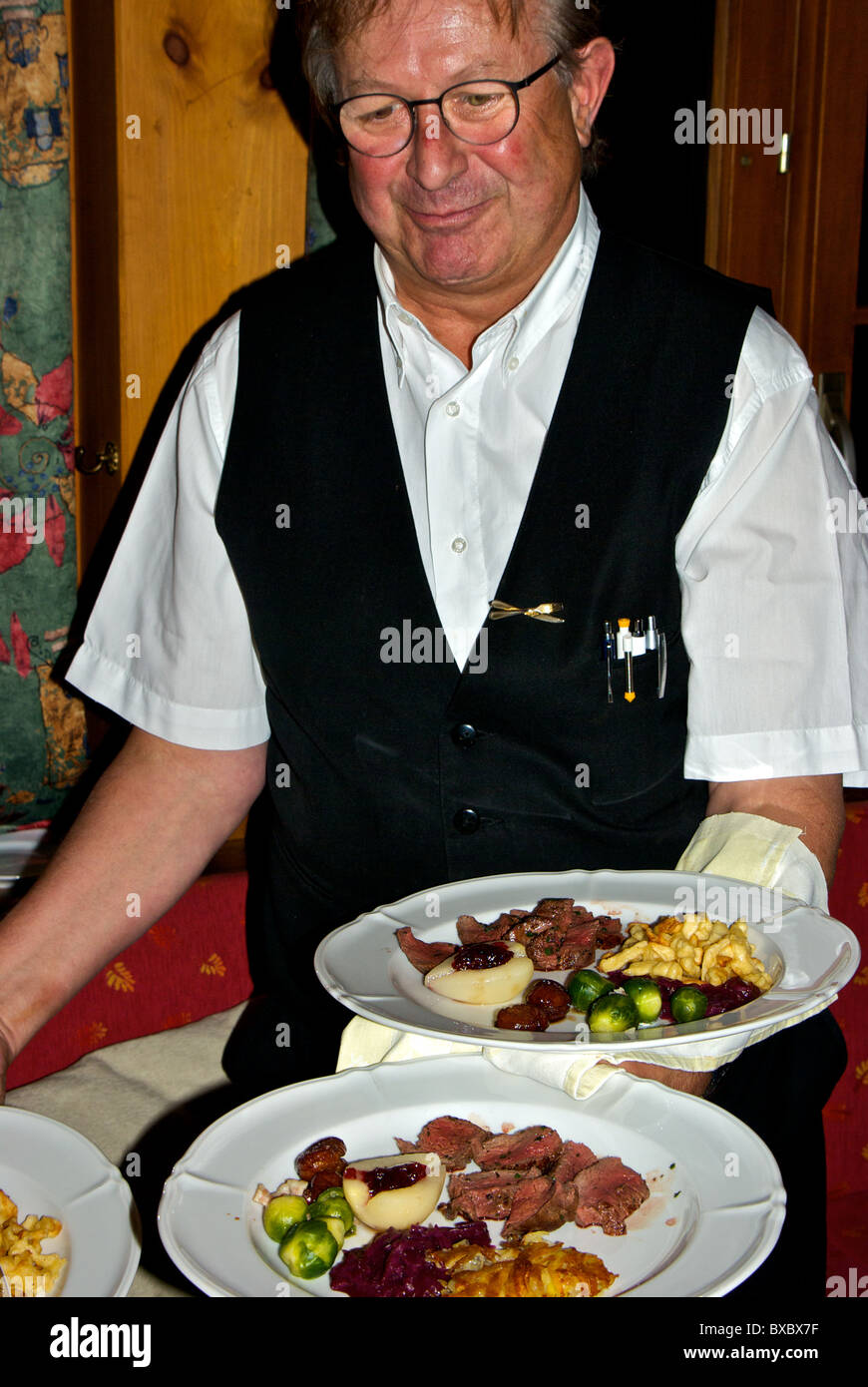 Restaurant Kellner servieren gebratene wilden Spiel Gams Filet Spätzle Brussel sprouts Rotkohl pochierte Birne Kandierte Kastanien Stockfoto