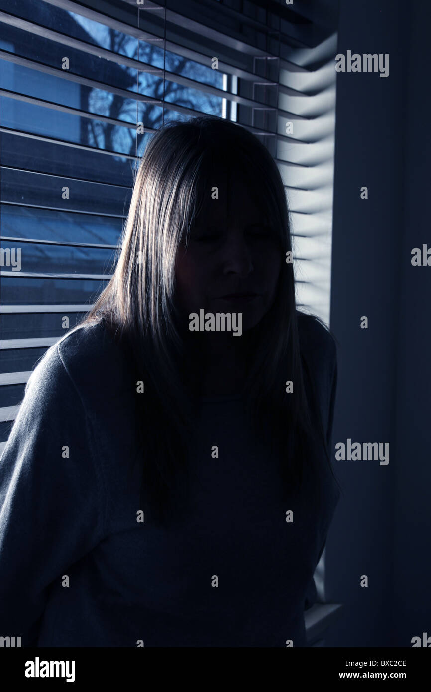 Porträt einer anonymen fair dunkelhaarige Frau sitzt mit dem Rücken zu einem hölzernen Fenster blind in der Nacht. Stockfoto