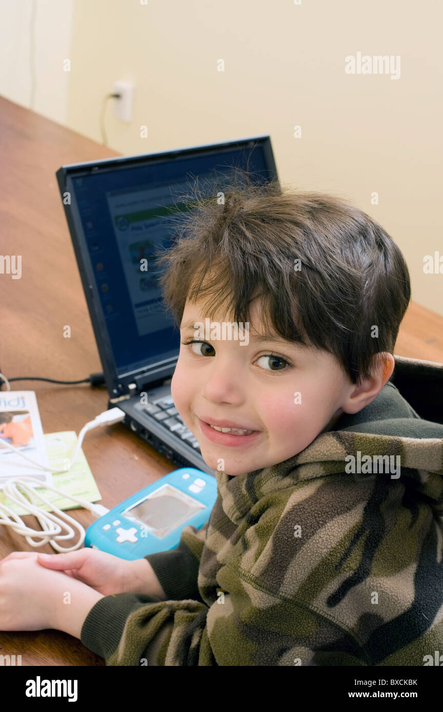 4 und 1/2 Jahre alten Hispanic junge verbindet seine Digi-handheld-Spiel mit seinen Eltern Computer Programme hochladen. -Modell veröffentlicht. Stockfoto