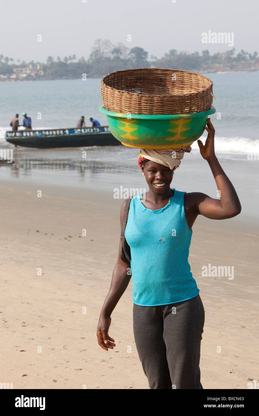 Es steht eine Frau mit einem Korb auf dem Kopf an den Stränden von Freetown, Sierra Leone, Westafrika. Stockfoto