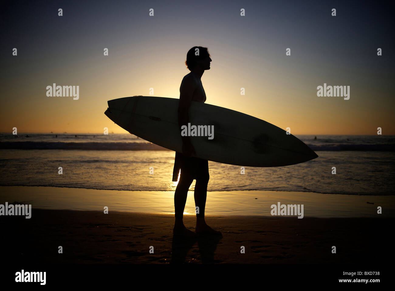 Silhouette der Surfer hält ein Surfbrett am Strand bei Sonnenuntergang. Stockfoto