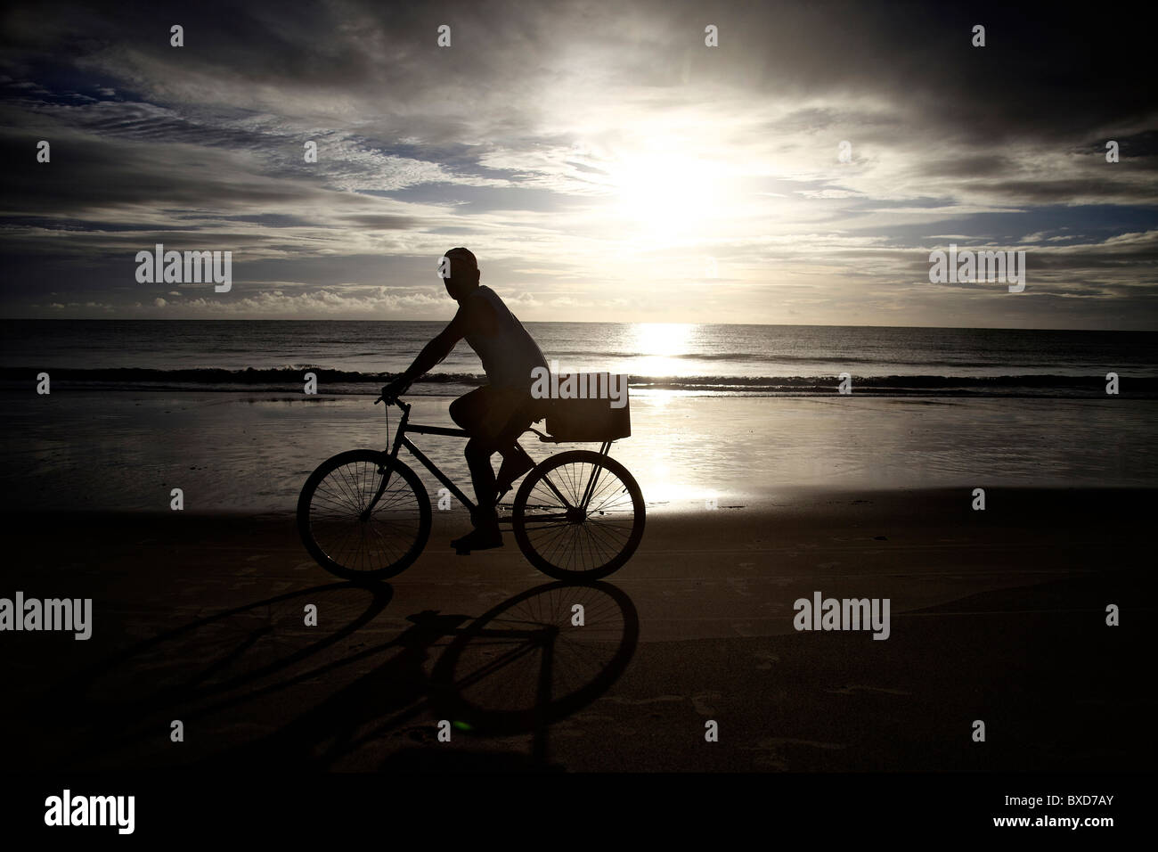 Ein Mann fährt Rad, am Strand bei Sonnenaufgang zu arbeiten. Stockfoto