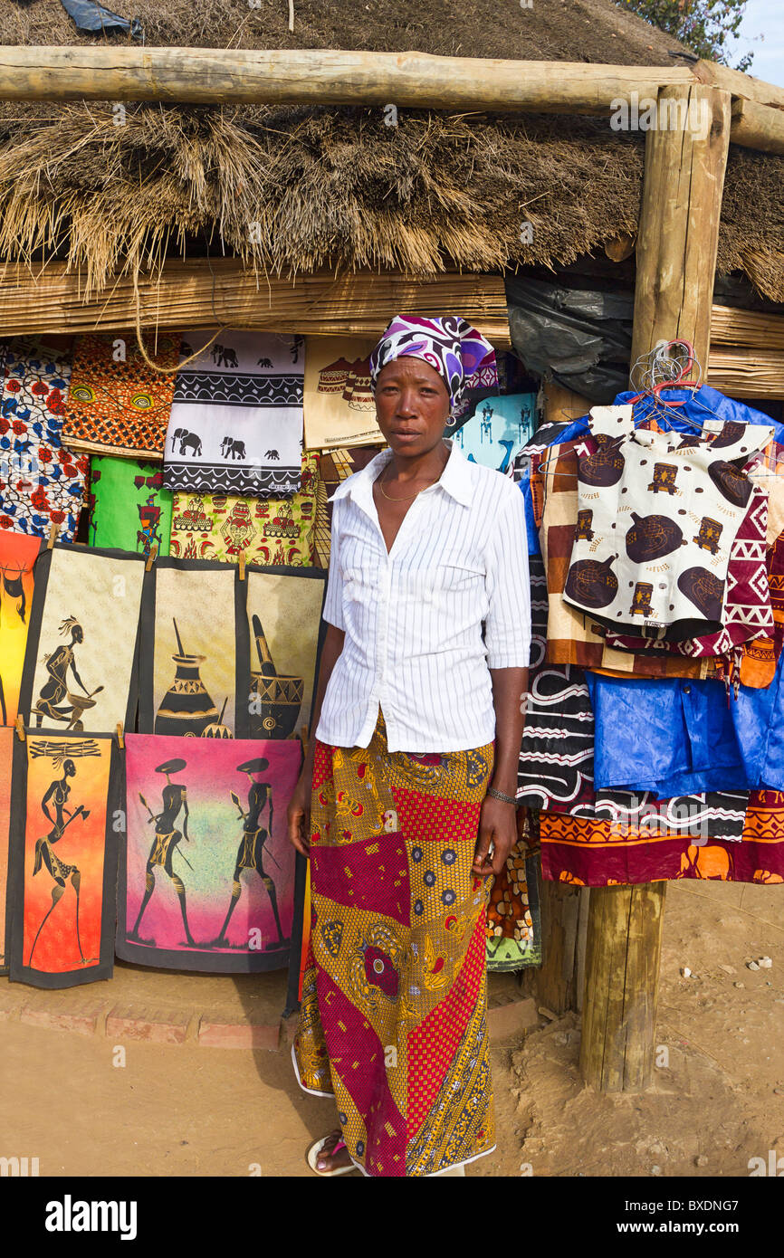 Lokale einheimische Frau steht mit einem bunten Tuch zum Verkauf an Handwerksdorf in Lusaka, Sambia, Afrika Stockfoto