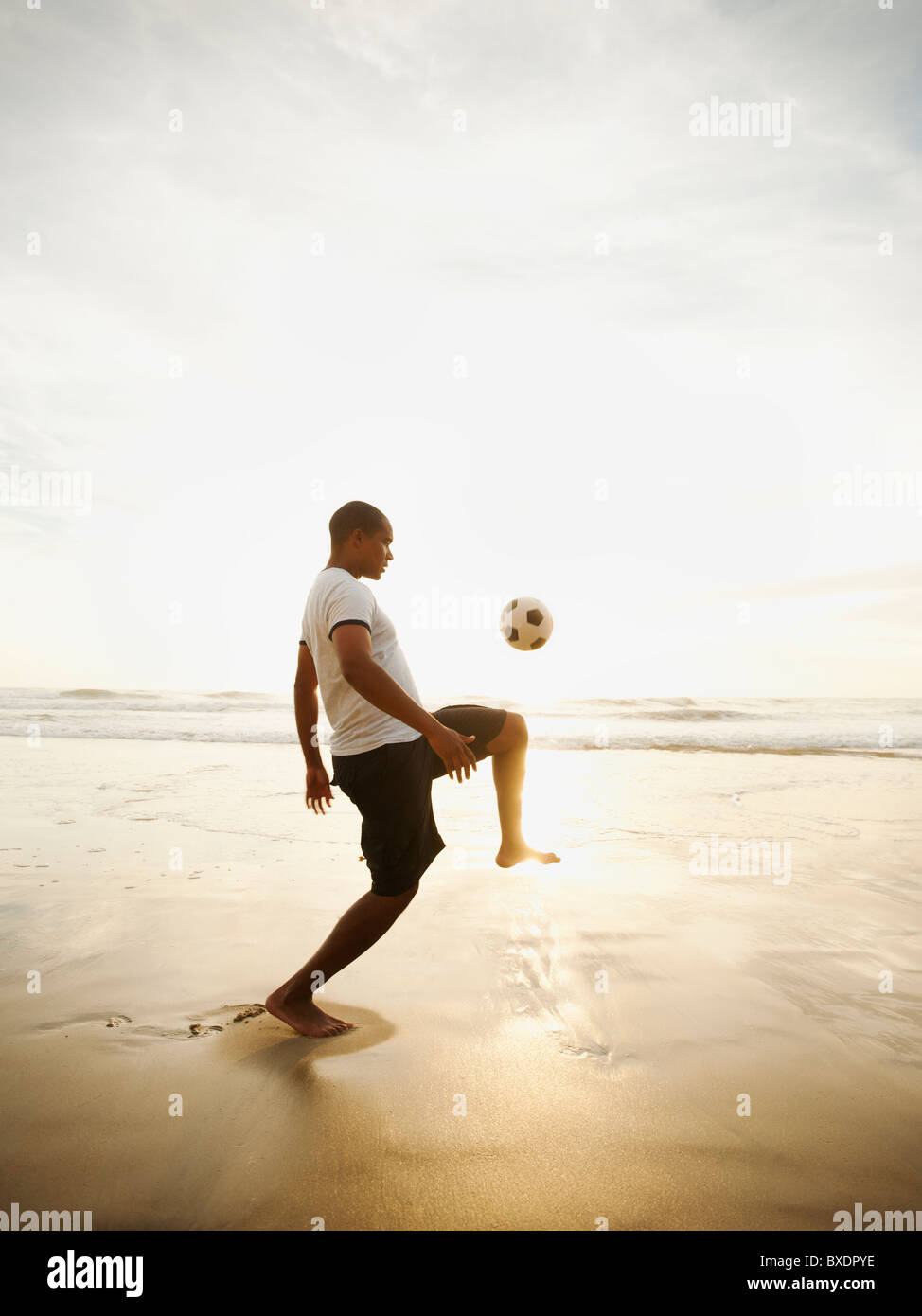 Schwarzer Mann mit Fußball spielen am Strand Stockfoto