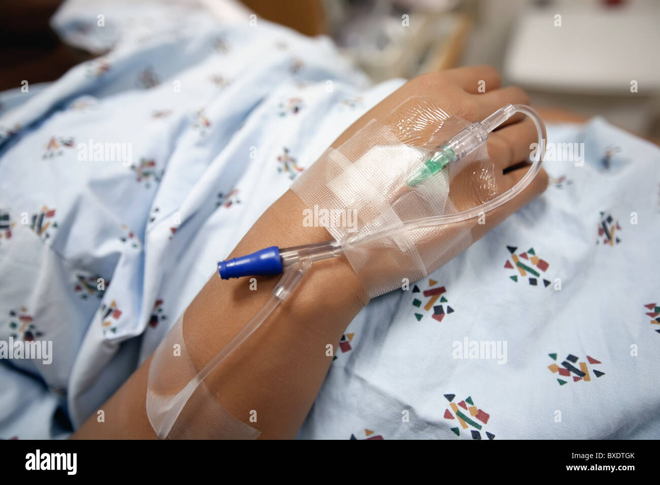 Frau trägt ein Krankenhemd mit einer IV-Leitung und Katheter zur Hand. Stockfoto