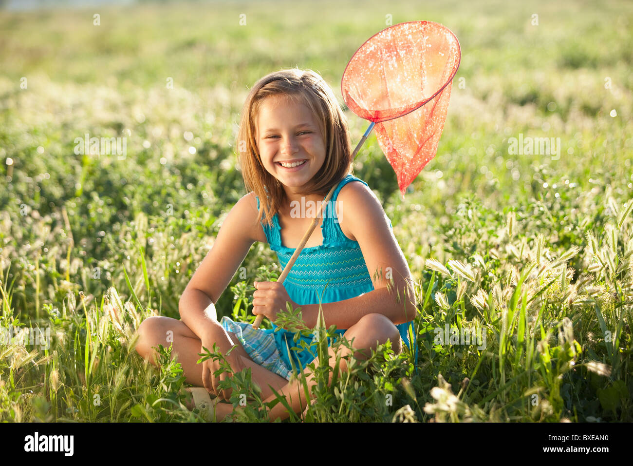 Junges Mädchen sitzen im Feld mit einem Schmetterlingsnetz Stockfoto