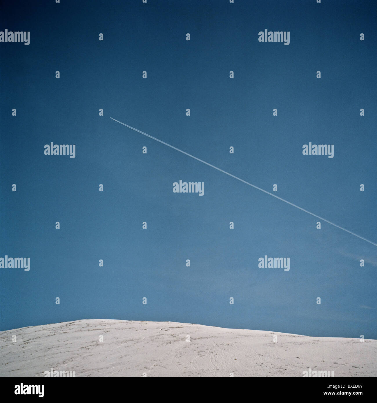 Die minimalistische Landschaft zeigt eine Flugdampfspur über einem blauen Himmel über den verschneiten Campsie Fells. Stockfoto