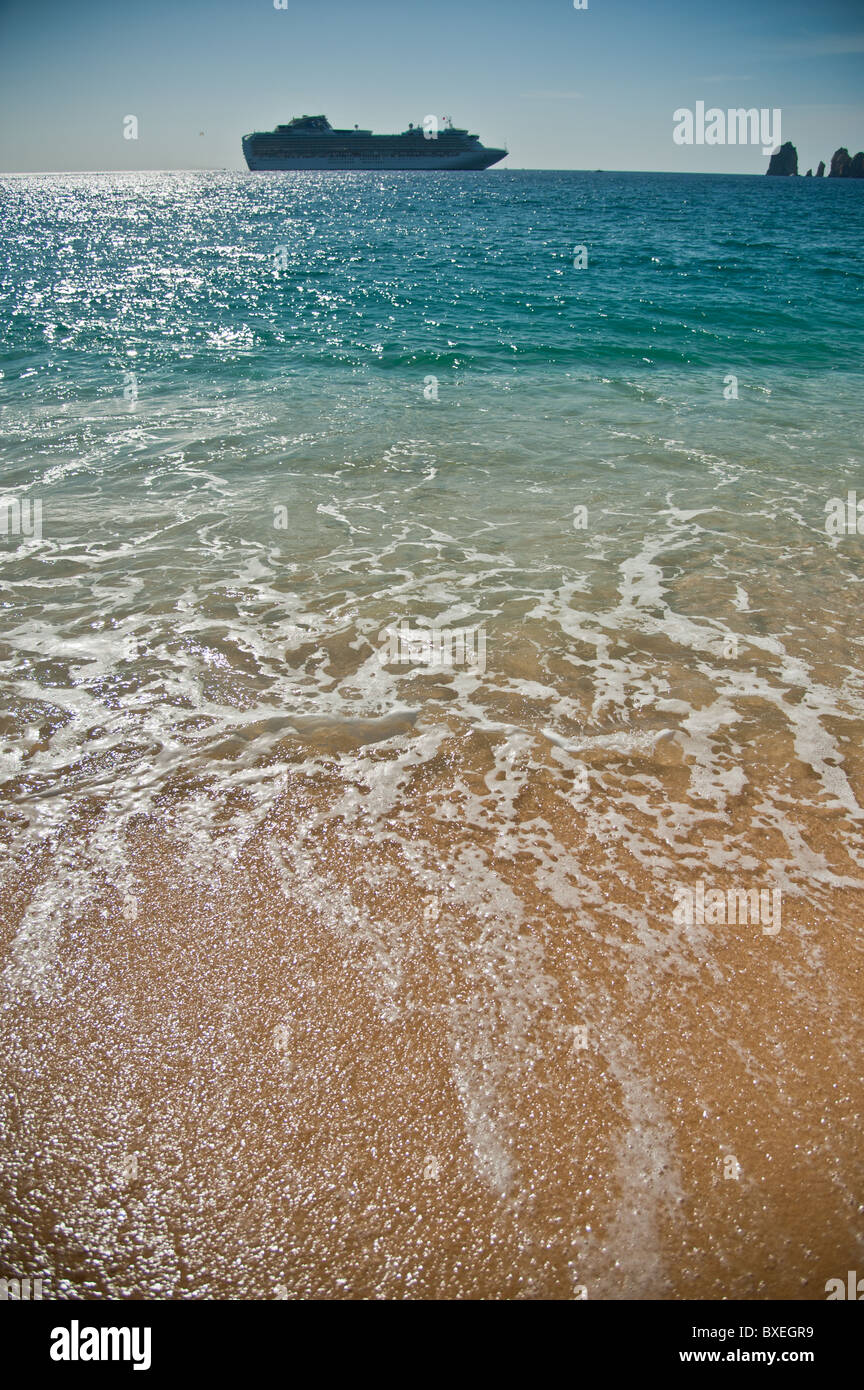 Sanfte Wellen brechen auf einer tropischen Sandstrand mit einem Kreuzfahrtschiff auf entfernten Horizont Stockfoto