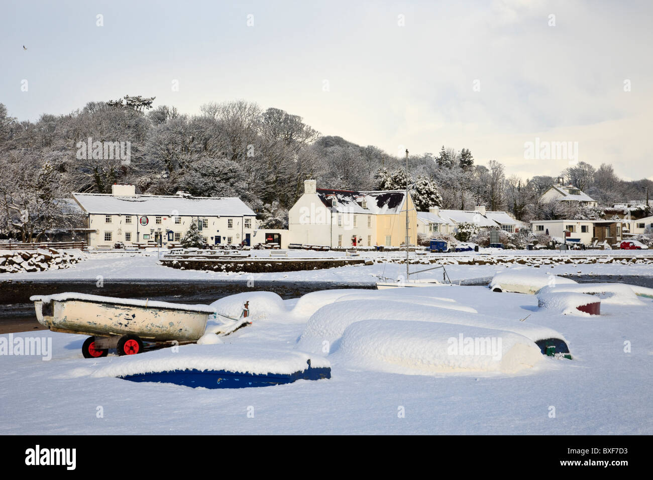 Red Wharf Bay (Traeth Coch), Isle of Anglesey, North Wales, UK, Europa. Schnee-Szene mit umgedrehten Booten an der Küste im winter Stockfoto