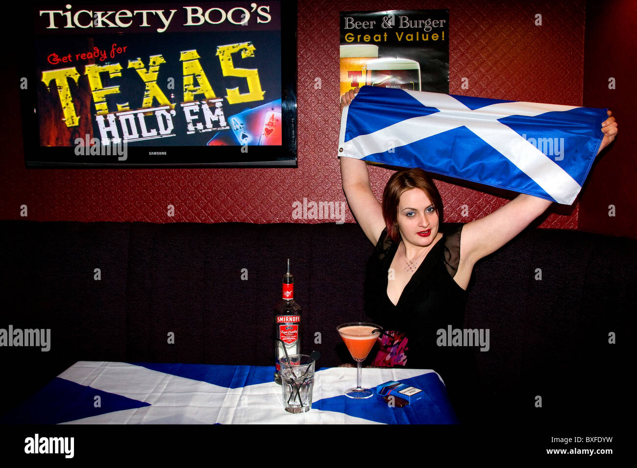 Glamouröse Frau sitzt an einem Tisch mit Getränken und winkte der schottischen St. Andrews Flagge in einem örtlichen Pub in Dundee, Großbritannien Stockfoto