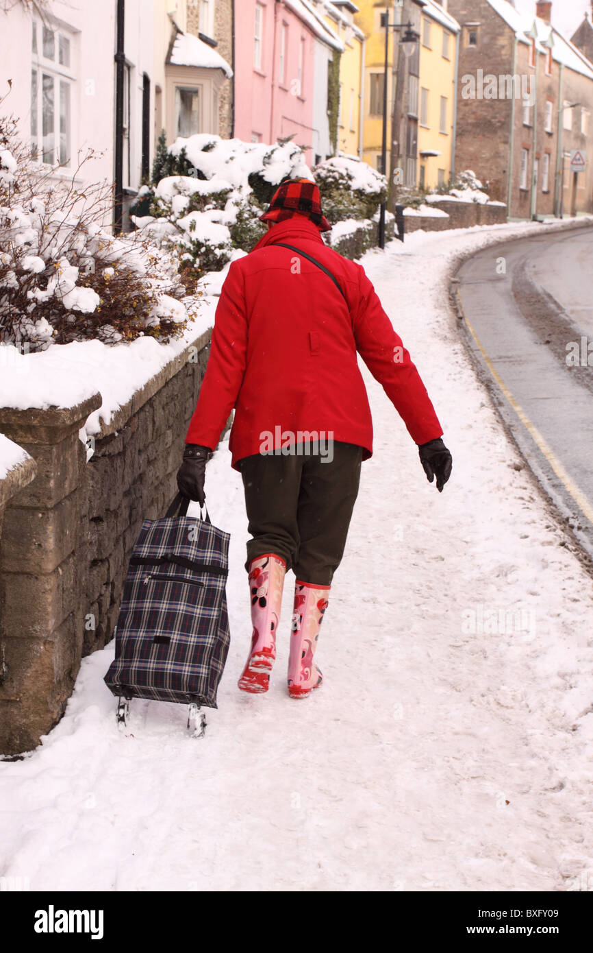 Frau zu Fuß auf dem Bürgersteig mit Einkaufswagen in Wells, Somerset Dezember 2010 winter Schnee Stockfoto