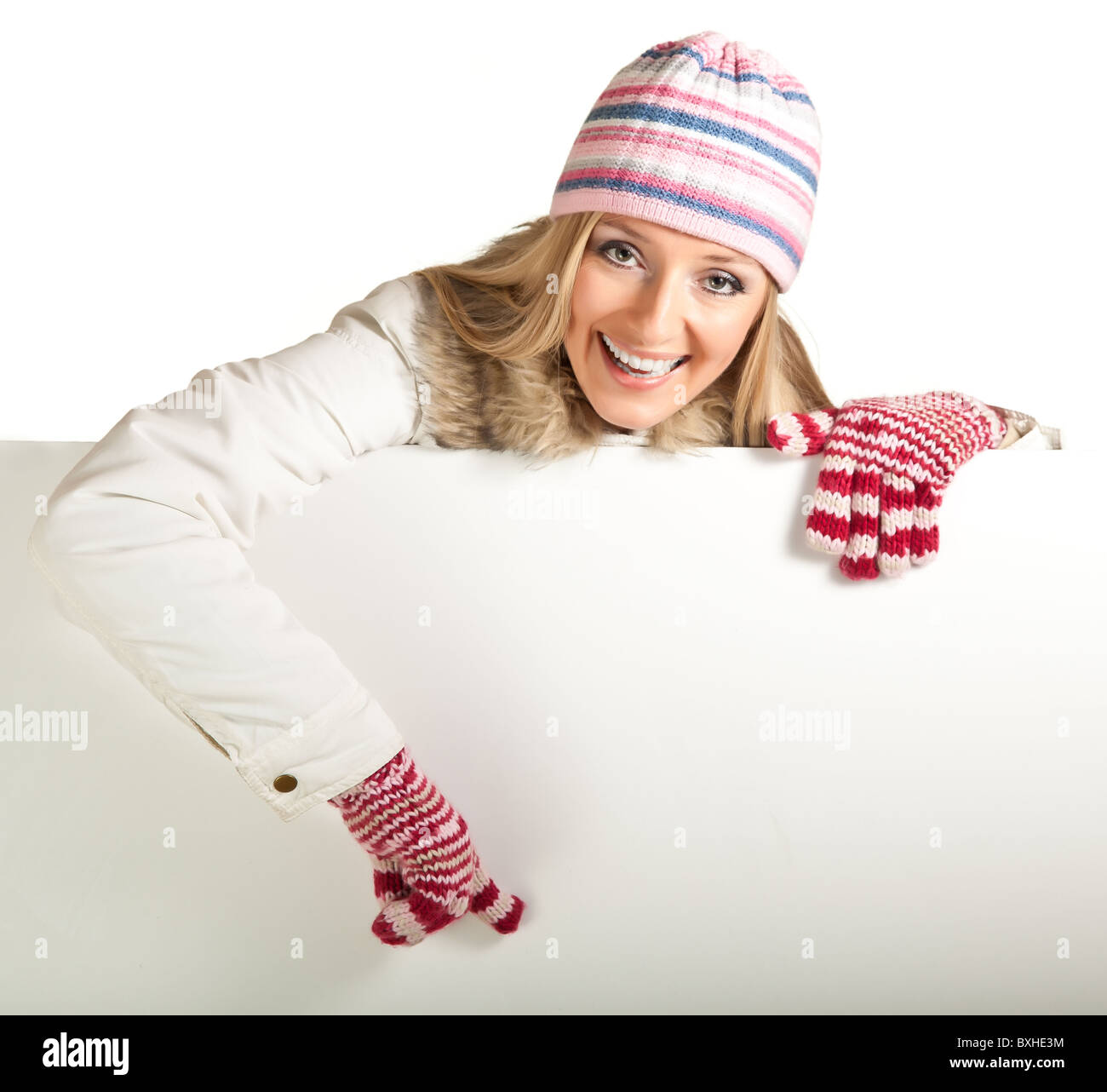 Frau in bunte Mütze und Handschuhe lugt hinter Whiteboard isoliert auf weiss Stockfoto