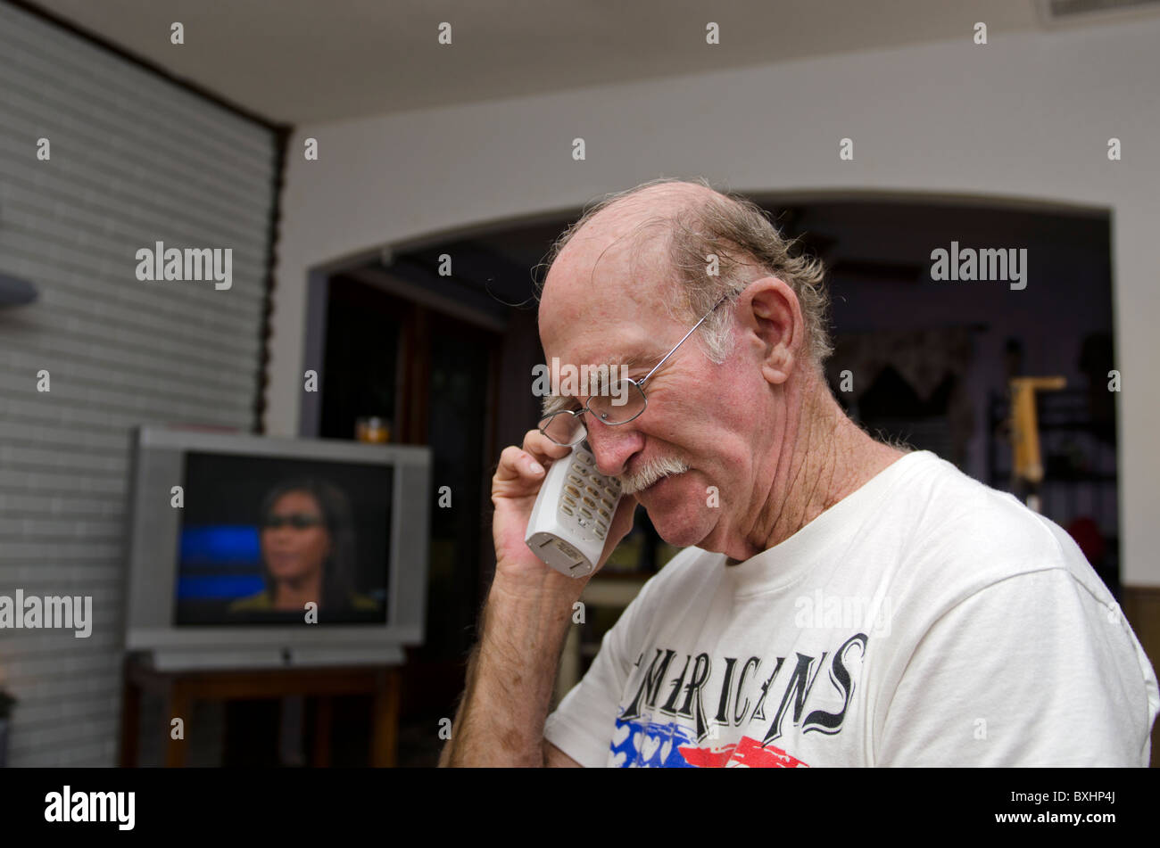 Ein senior kaukasischen Mann lächelt, als er spricht über ein schnurloses Telefon in seinem Haus. Stockfoto