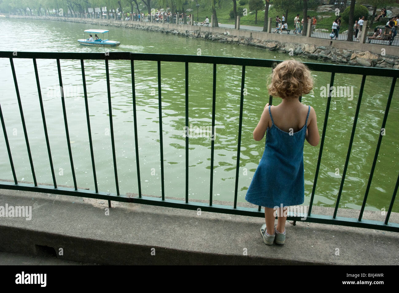 Blondes Mädchen steht die Schiffe durch die Geländer auf dem See in Behai Park, Peking, China zu beobachten. Stockfoto