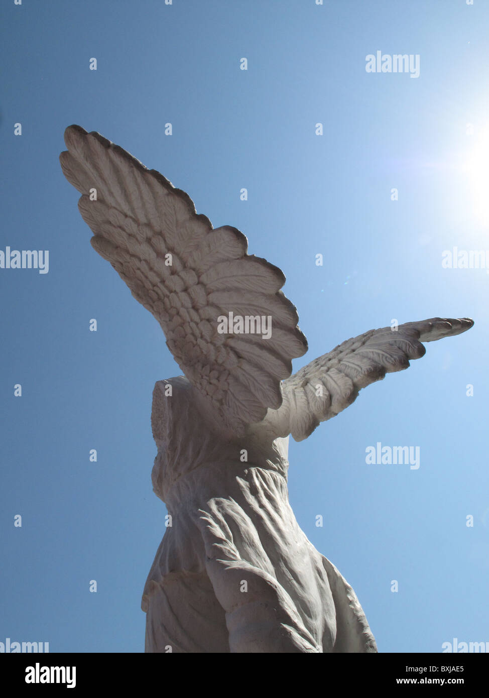 konkrete Steinfigur Engel gegen blauen Himmel Flare Sonne fliegen Skulptur Stockfoto