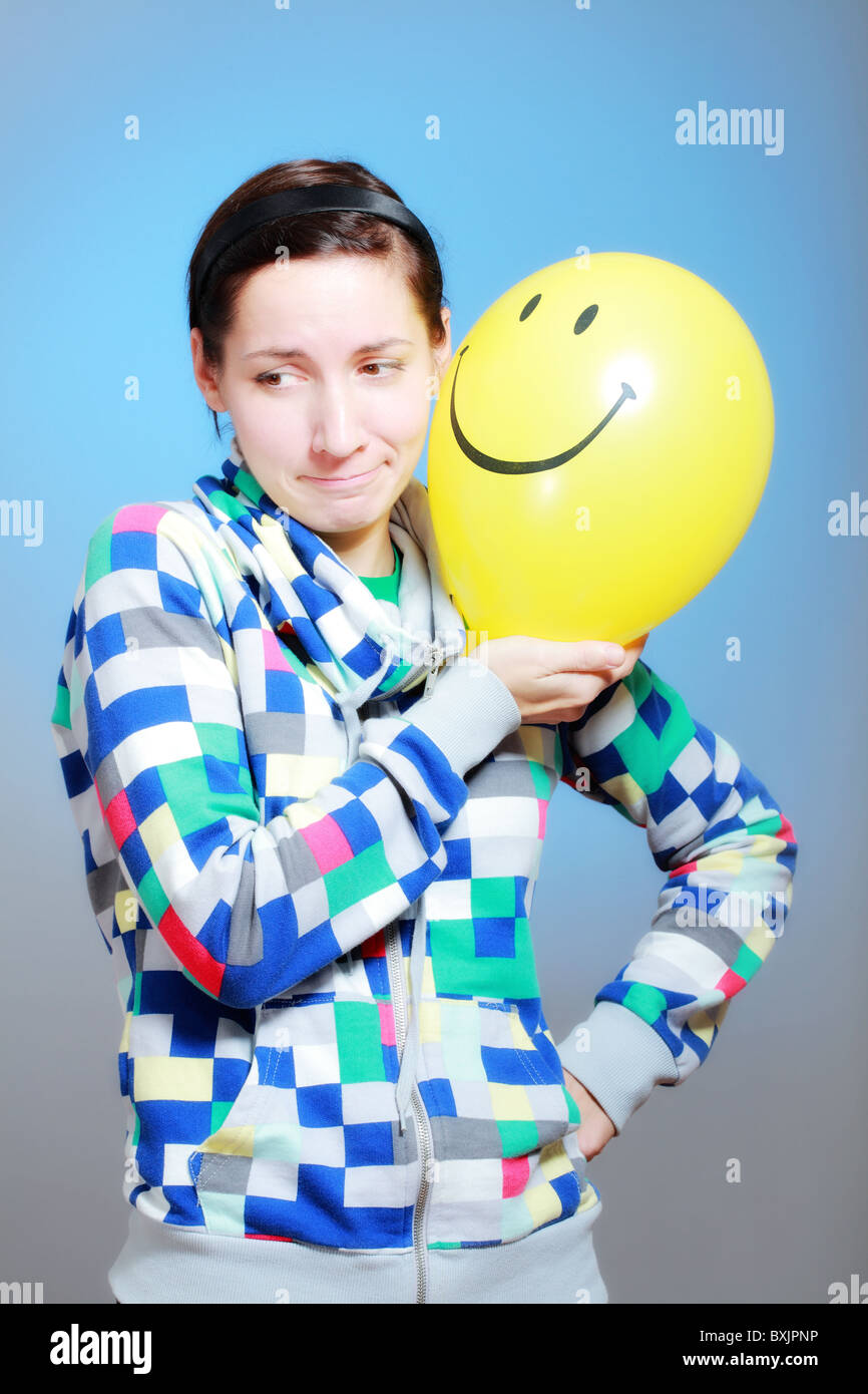 Mädchen mit einem gelben Smiley Ballon gegen blau Stockfoto