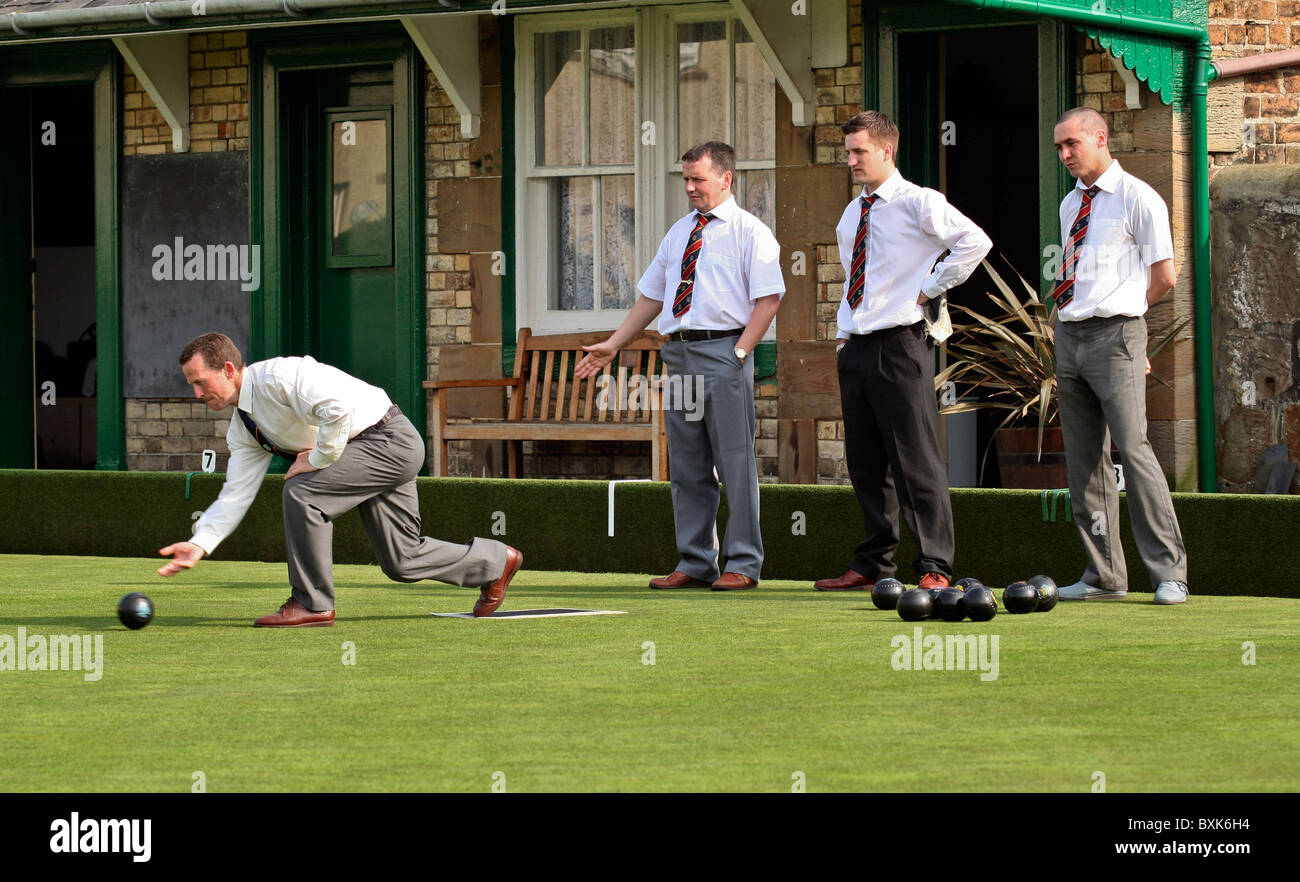 Ein Mann rollt eine Schüssel während eines Wettkampfes Rasen-Bowling, während seine Mannschaftskollegen schauen auf Stockfoto