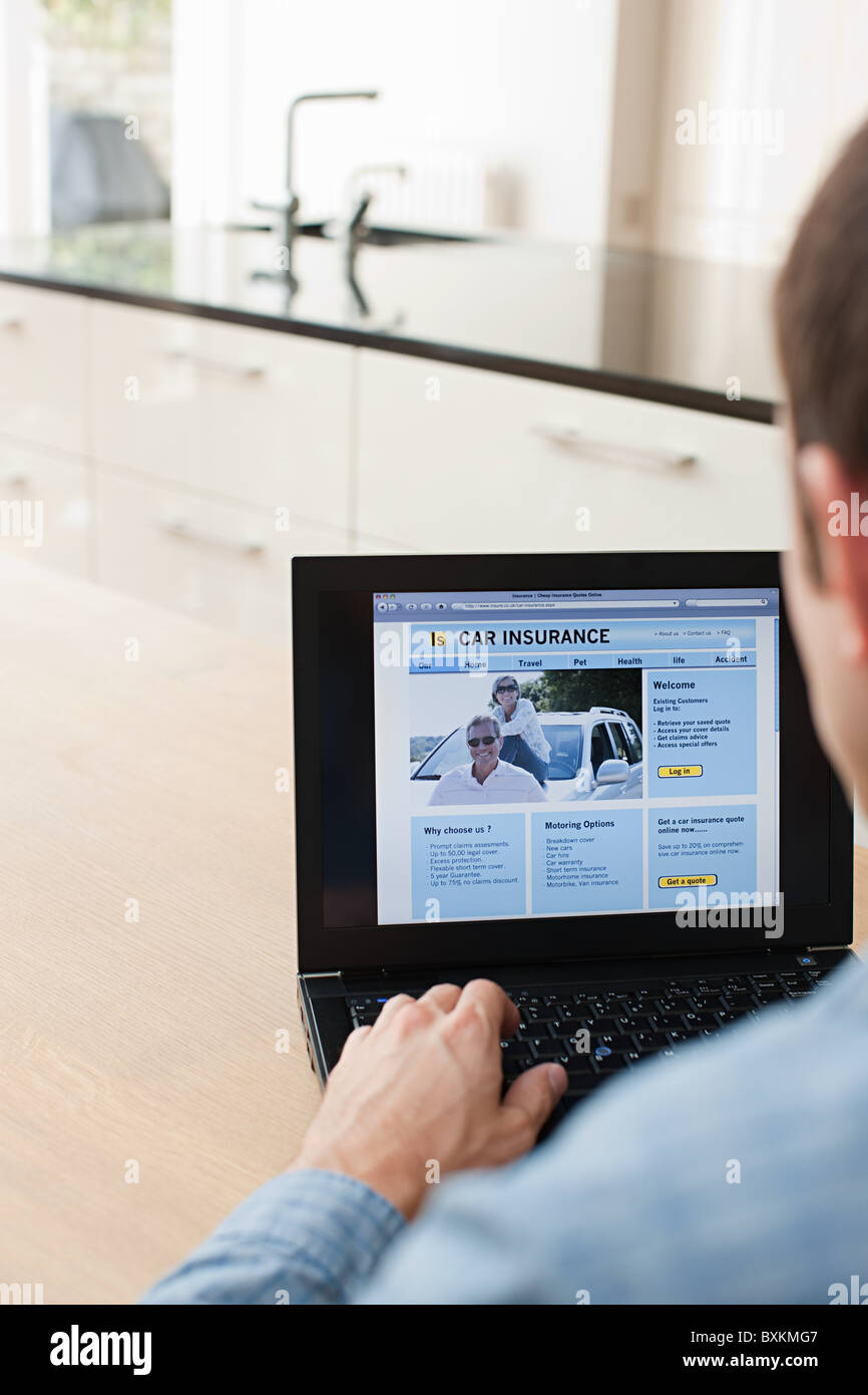 Junger Mann, Blick auf Kfz-Versicherung auf laptop Stockfoto