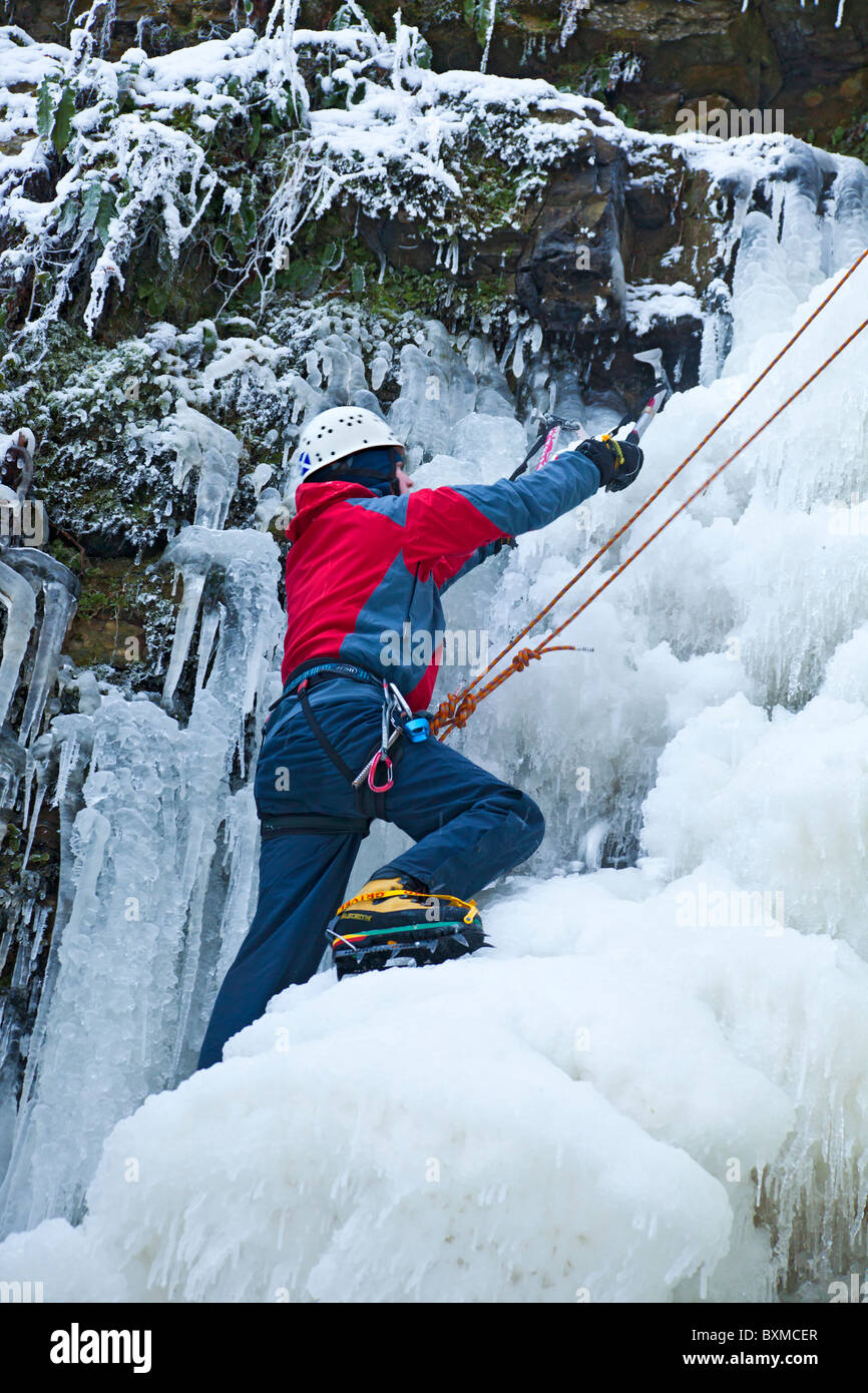 Männliche Bergsteiger wird während einer Eisklettern auf einem gefrorenen Wasserfall (Lynn fällt) außerhalb Dalry in North Ayrshire, Schottland gesichert. Stockfoto
