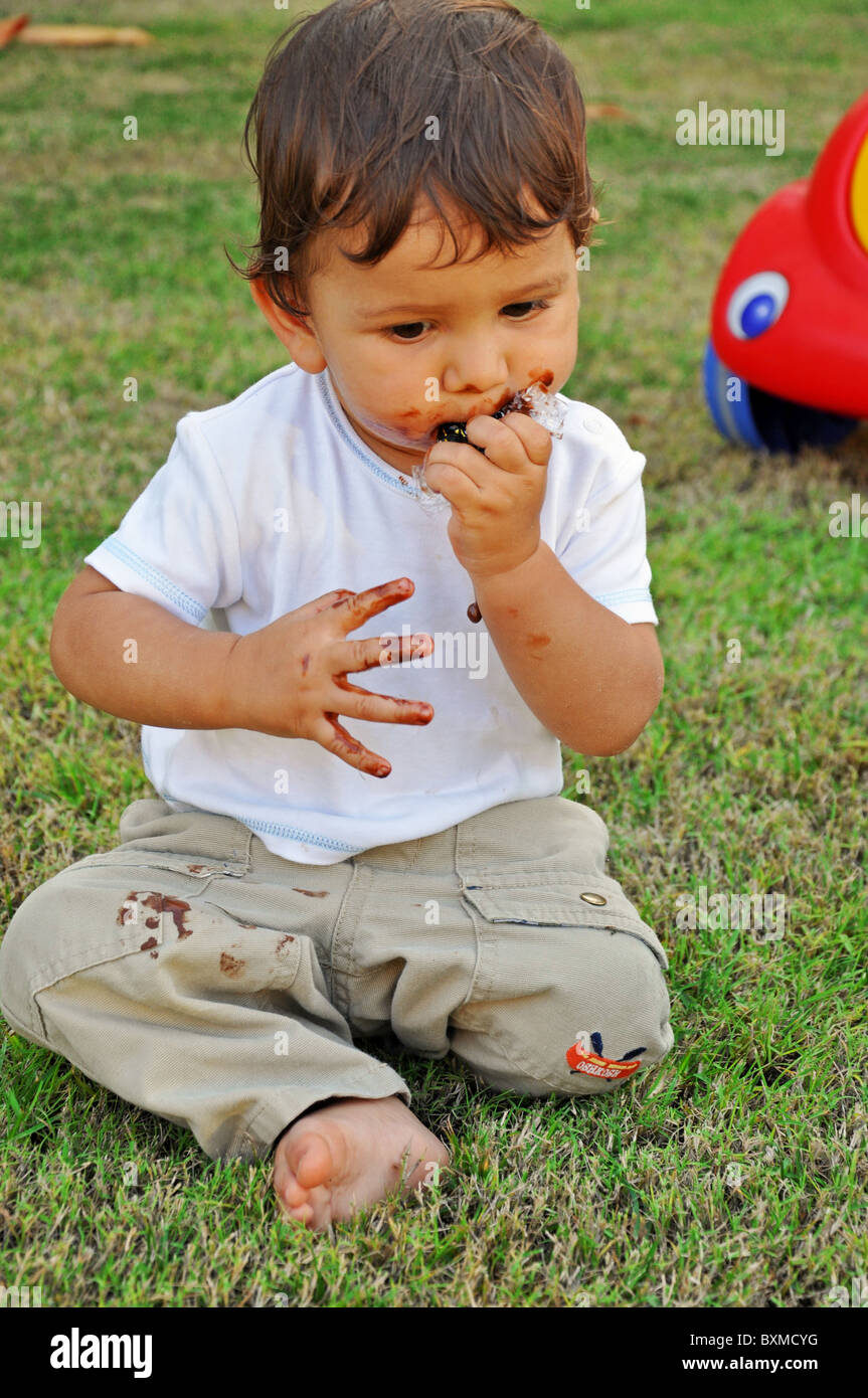 Ein Jahre alter Junge, Schokolade zu essen, auf dem Rasen Stockfoto