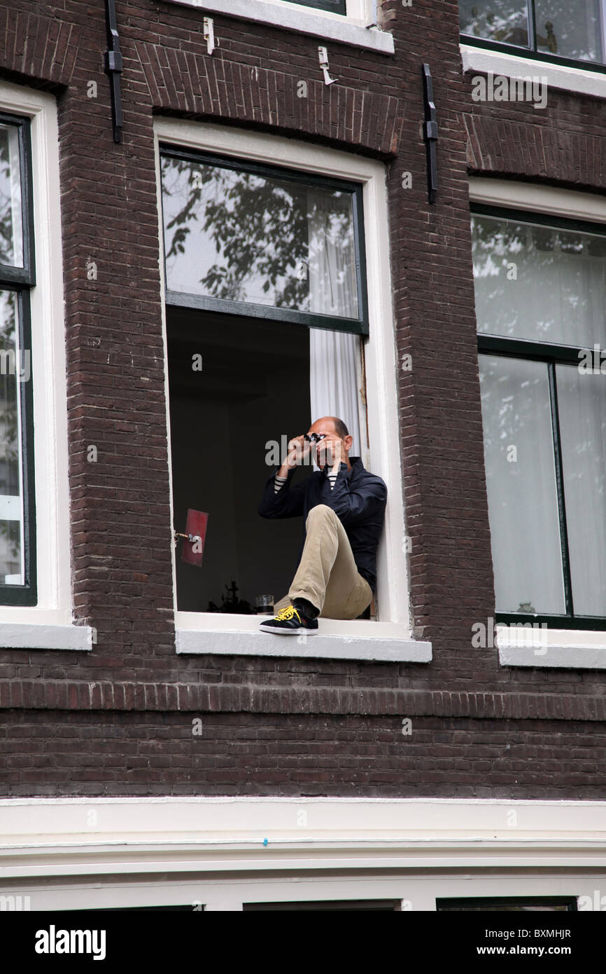 Mann, der im Fensterbrett sitzt, um Gay Pride Amsterdam zu beobachten Stockfoto