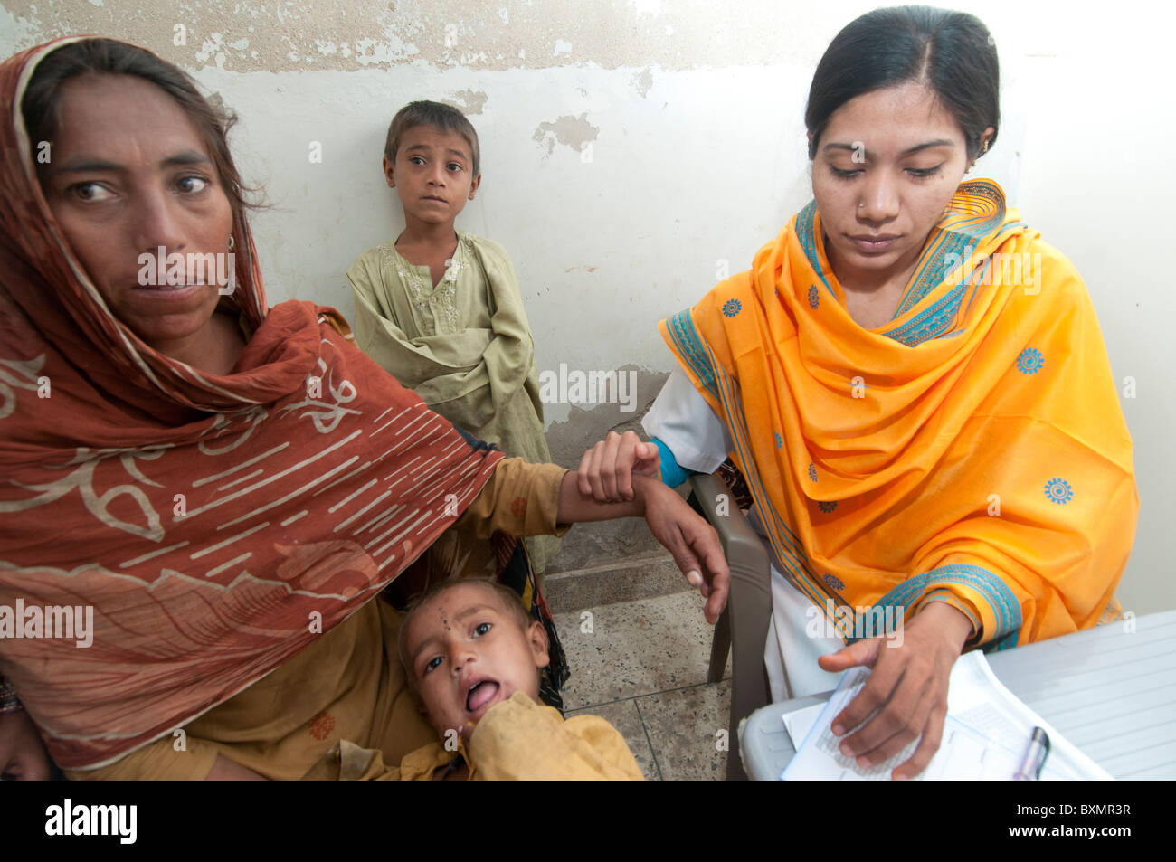 Pakistan nach der Flut. Arzt Sahira Bano untersucht einen Patienten beobachtet von ihrer Familie, sie nimmt den Puls Stockfoto