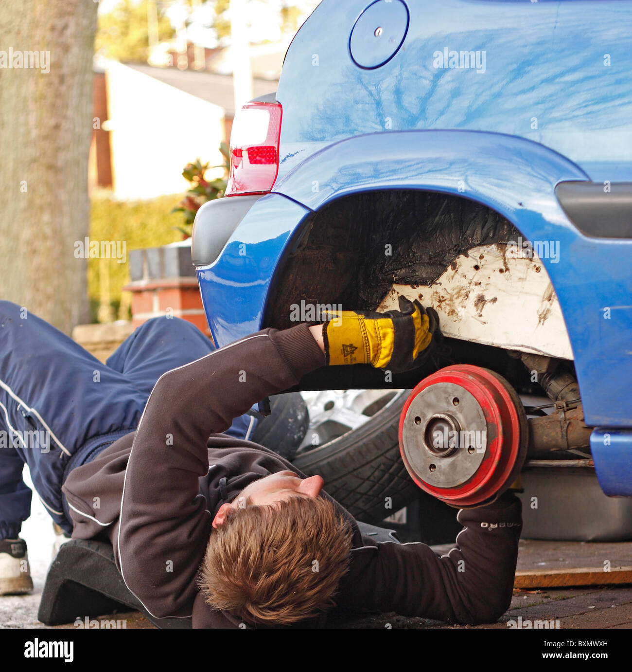 Ein Teenager männlich arbeiten unter einem Auto Reparatur Chassis/Radlauf. Rad entfernt und Auto aufgebockt. Stockfoto