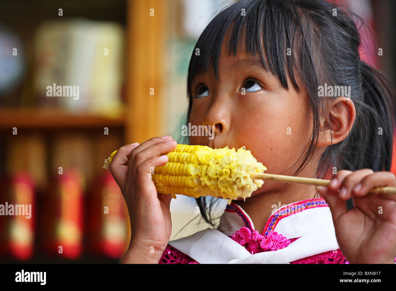 Junge Naxi-Chinesin, die Mais isst, Lijiang, China Stockfoto
