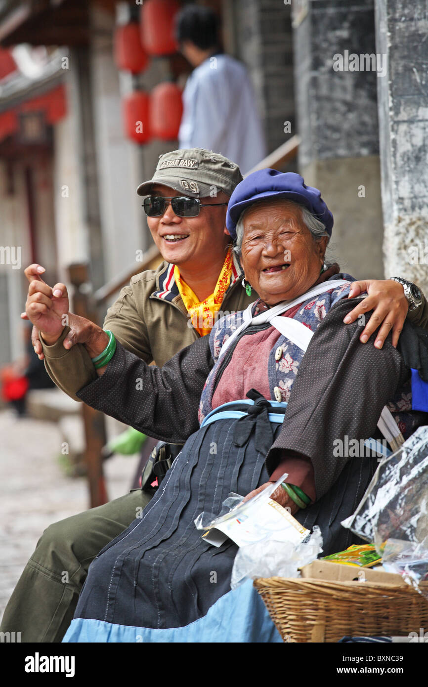 Naxi Frau posiert mit chinesischen Touristen, Lijiang, Provinz Yunnan, China Stockfoto