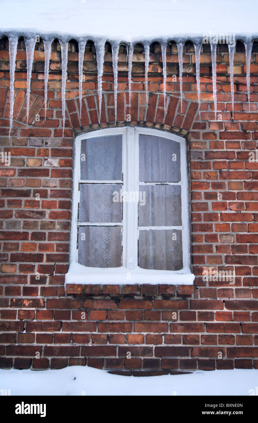 Großen Eiszapfen hängen über einem alten traditionellen Ziegel-Haus und ein Fenster Stockfoto