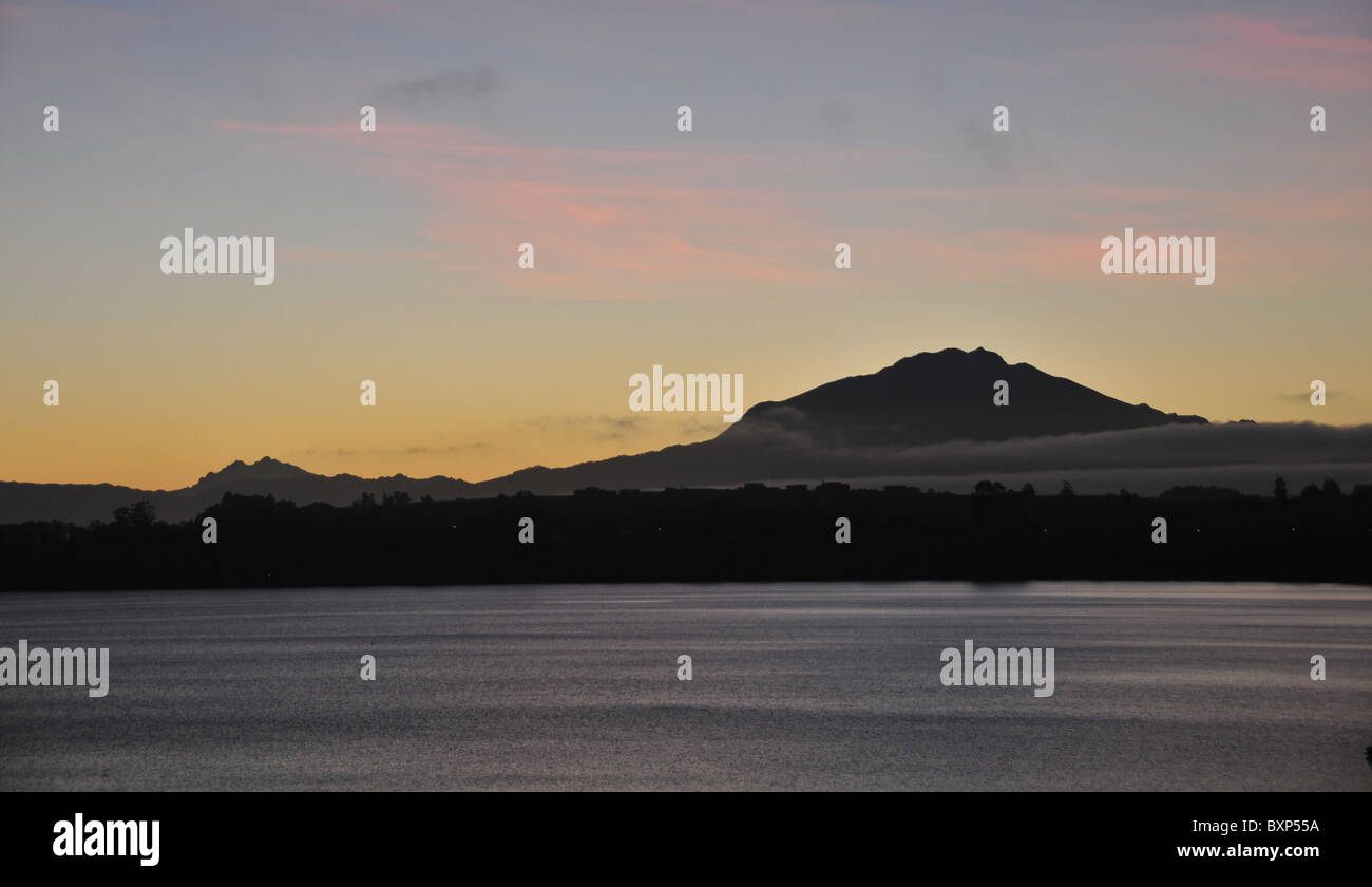 Rosa Wolken über die Morgendämmerung Silhouette des Volcan Calbuco, gesehen von Puerto Varas aus über das graue Meer See Llanquihue, Chile Stockfoto