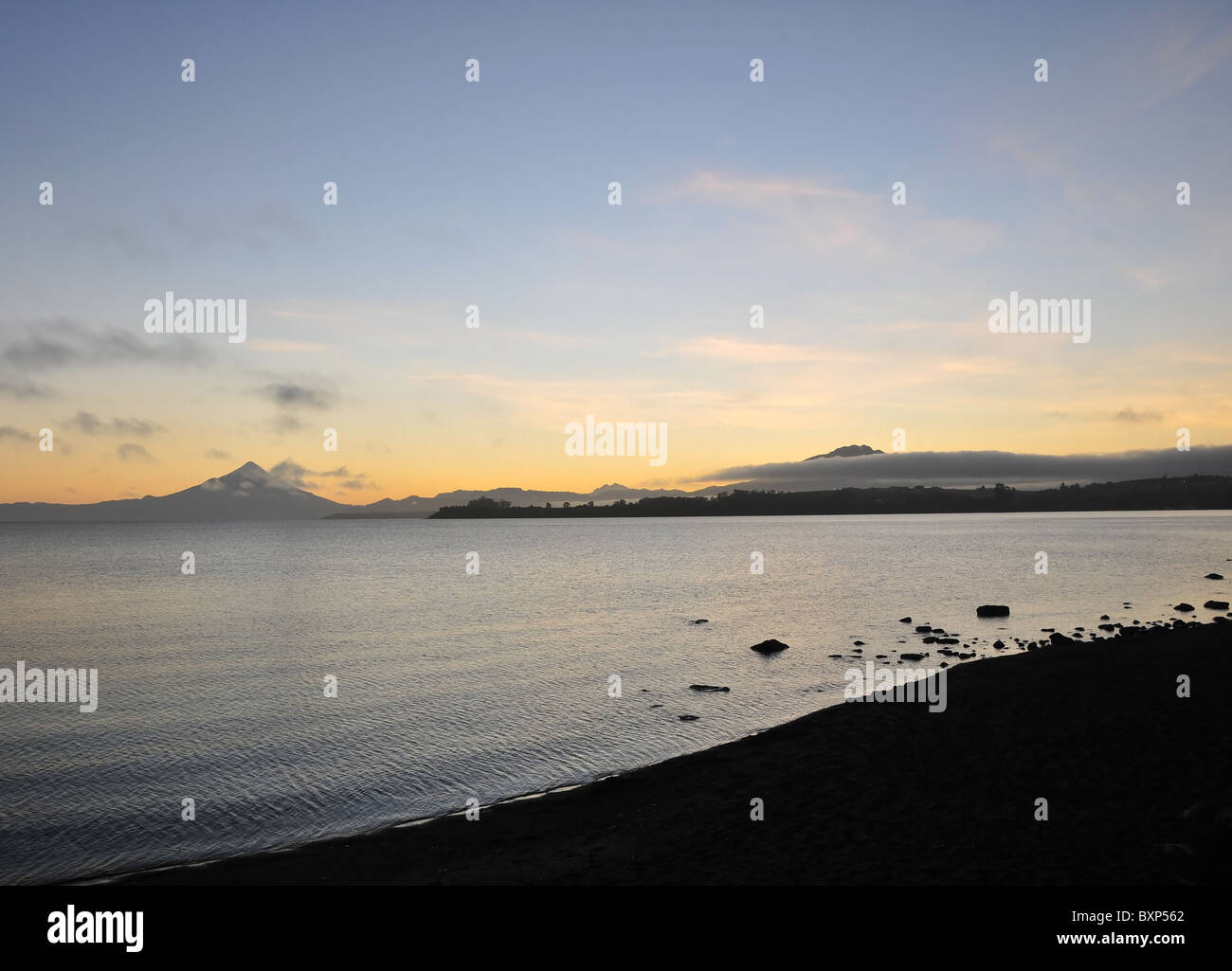 Dunklen Strand und See Llanquihue, Blick in Richtung Sonnenaufgang Wolken und Sonne glühen über Osorno und Calbuco Vulkane, Puerto Varas, Chile Stockfoto