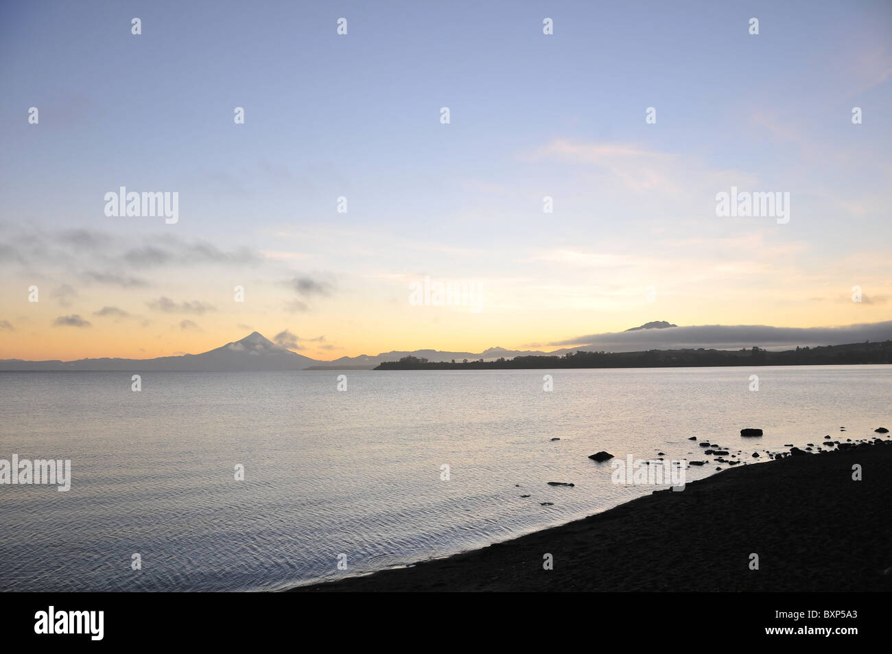 Llanquihue See Blick von einem dunklen Puerto Varas entfernt, einer Dämmerung Himmel gelb Sonne glühen über Osorno und Calbuco Vulkane, Chile Stockfoto