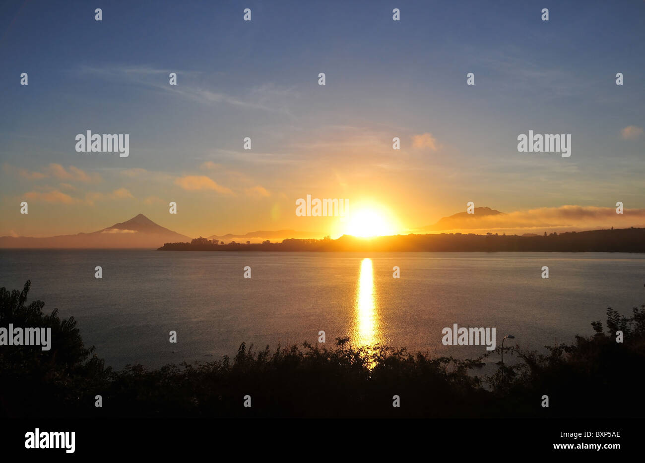 Gelbe Kugel von der aufgehenden Sonne auf See Llanquihue, Osorno bis Calbuco Vulkane, gesehen aus Puerto Varas, Chile Stockfoto