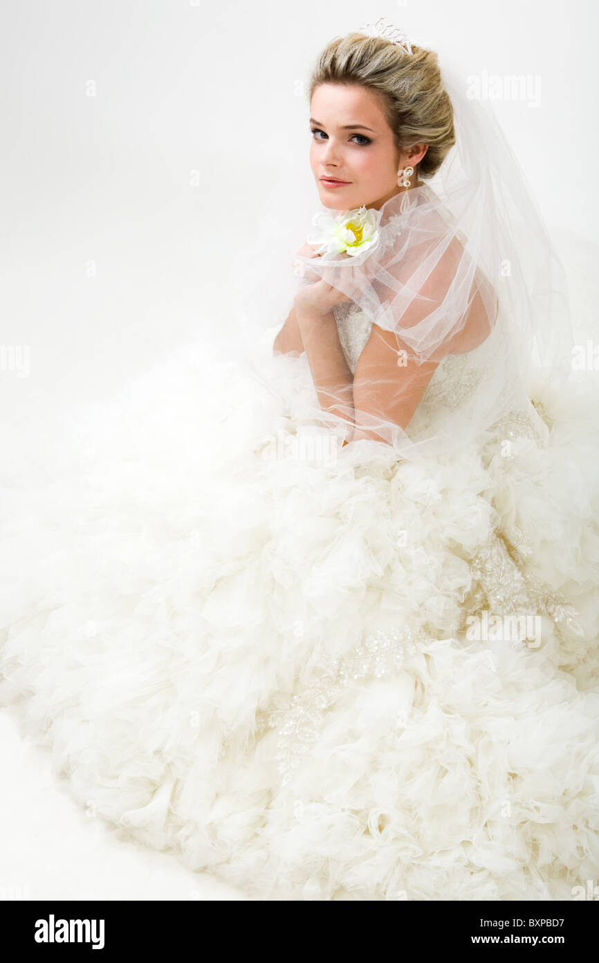 Foto von elegant Braut in modischen Ehe mit Blume in der hand sitzen und Blick in die Kamera Stockfoto