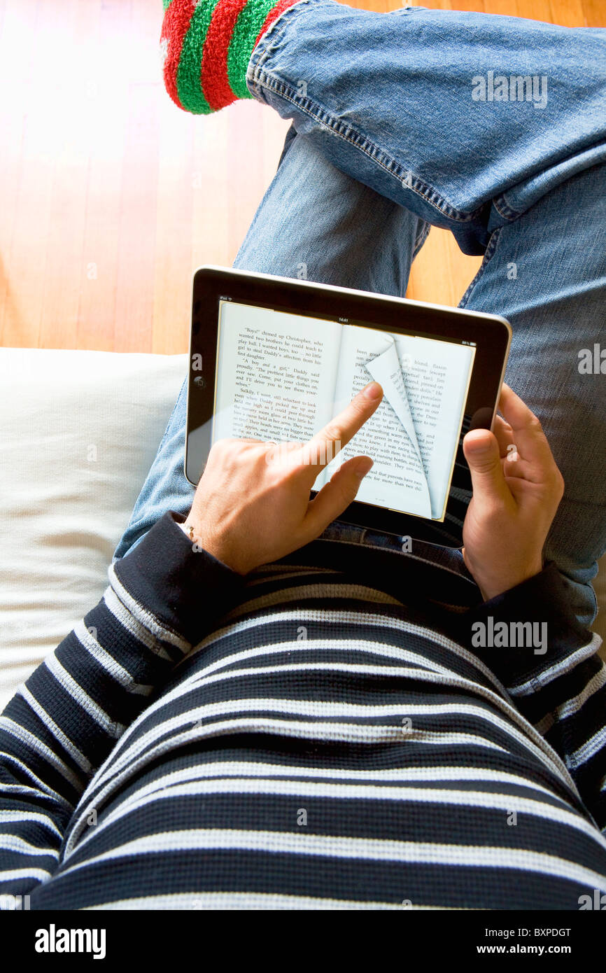 Mann Entspannung zu Hause mit einem Apple Mac iPad zum Lesen eines Buches von iBooks auf seinem Schoß. Stockfoto