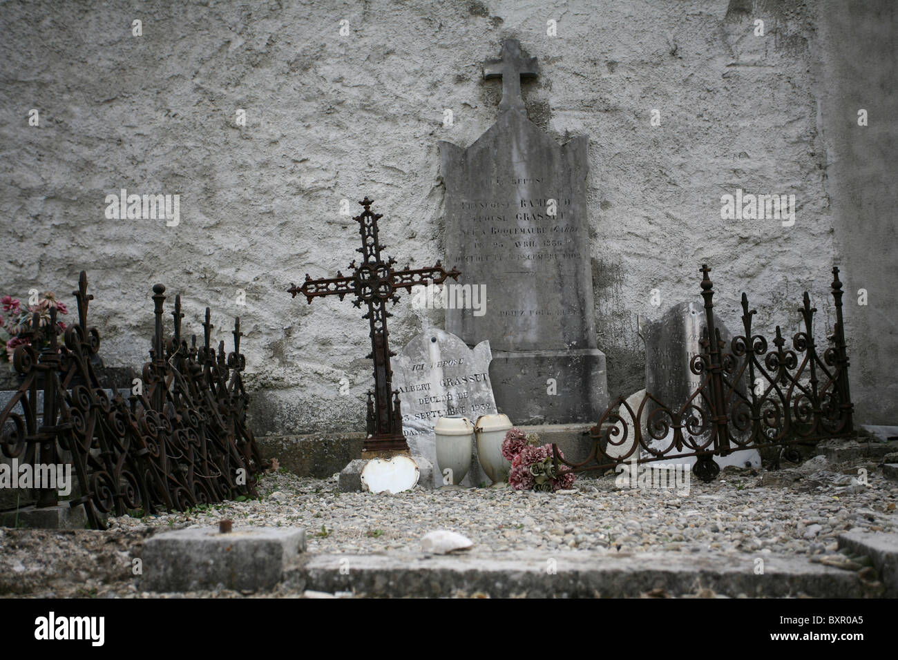 Eine Grabstätte mit gebrochenen Grabsteinen, kreuzen, Metallgeländer und Ornamente, gegen eine Wand in einem französischen Friedhof. Stockfoto