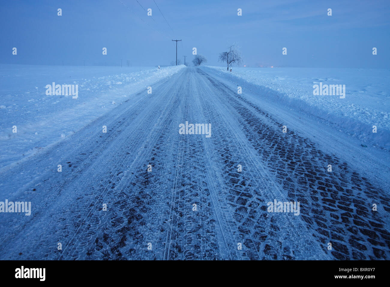 Tracks auf dem Schnee bedeckt Cobble Stone Landstraße am Abend Stockfoto