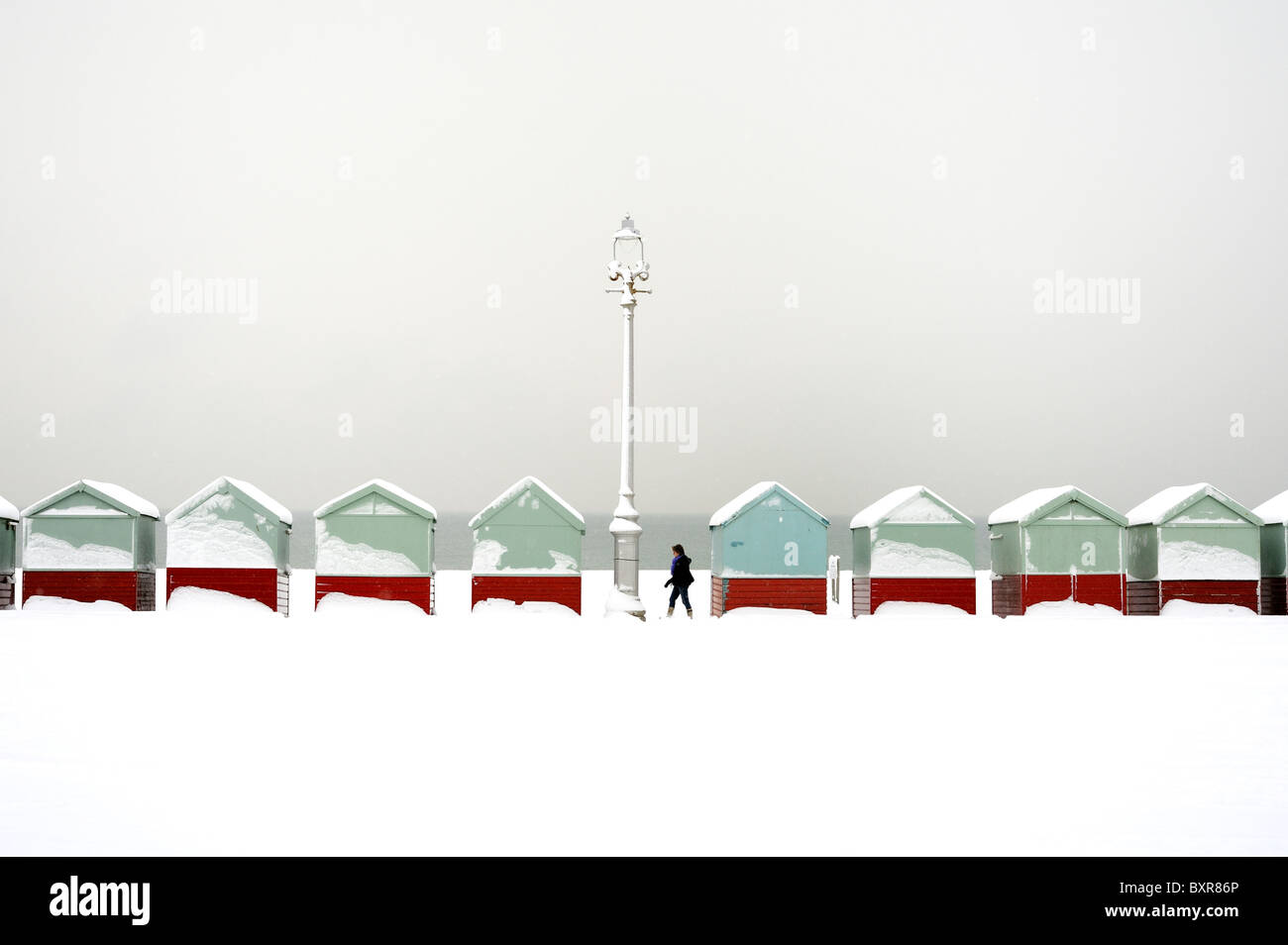 Ein Spaziergänger geht eine Reihe von Strandhütten mit Schnee bedeckt Stockfoto