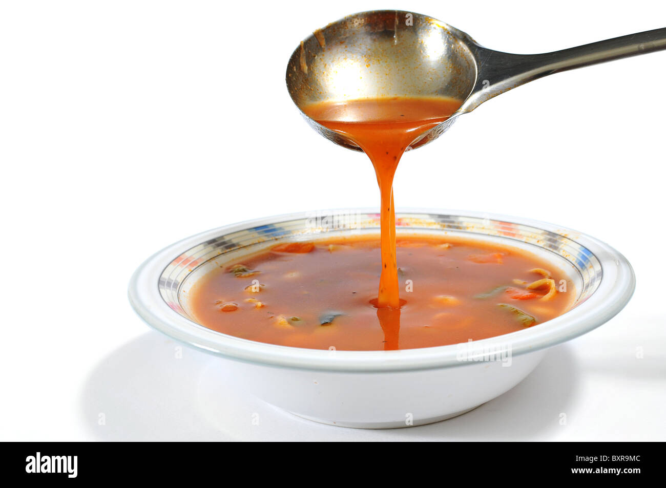 Minestrone-Suppe in eine Schüssel gießen, mit einer Schöpfkelle isoliert auf weiss Stockfoto