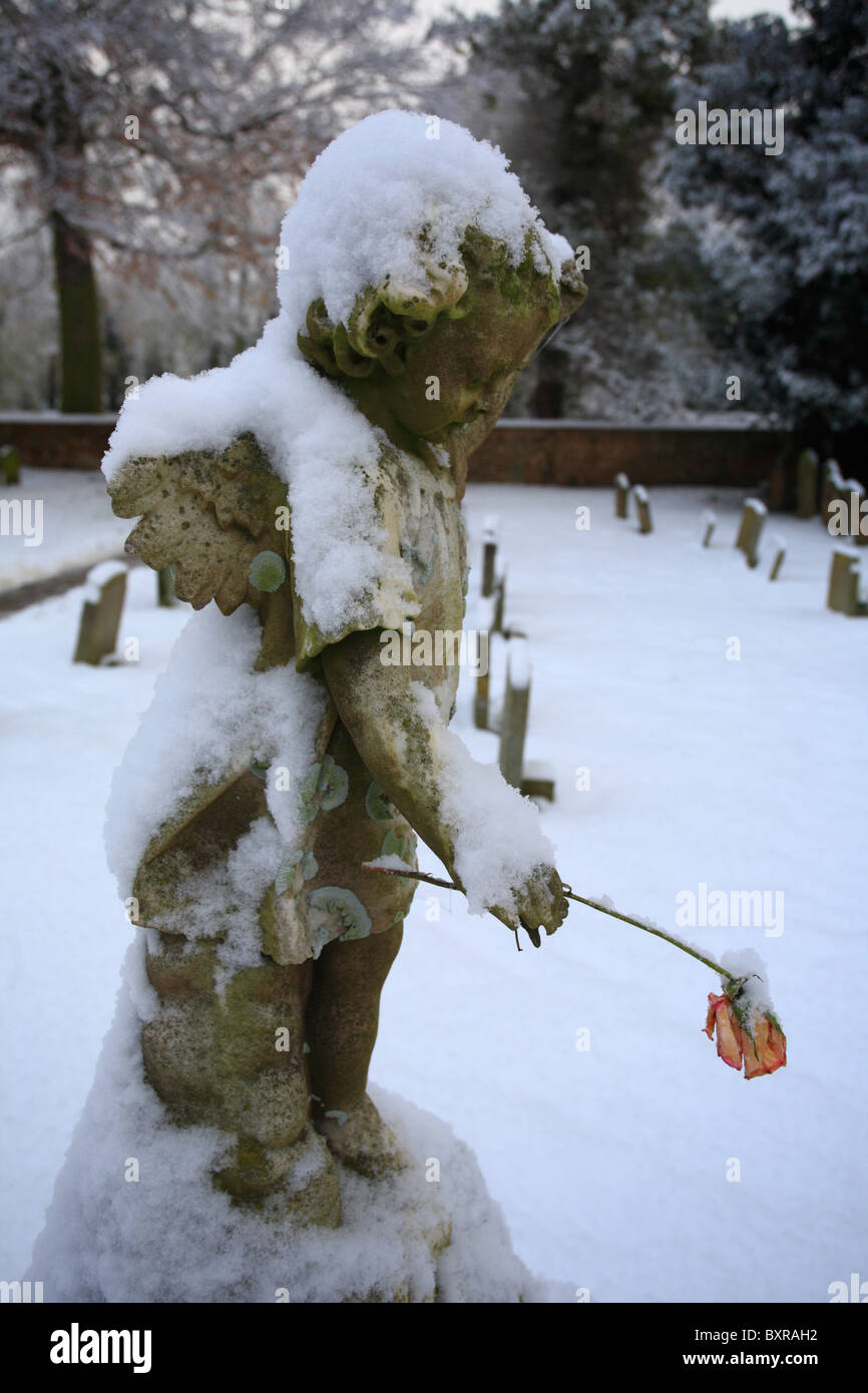Bild von einem Cherub/Engel, die eine Blume im Schnee auf einem Friedhof bedeckt. Stockfoto