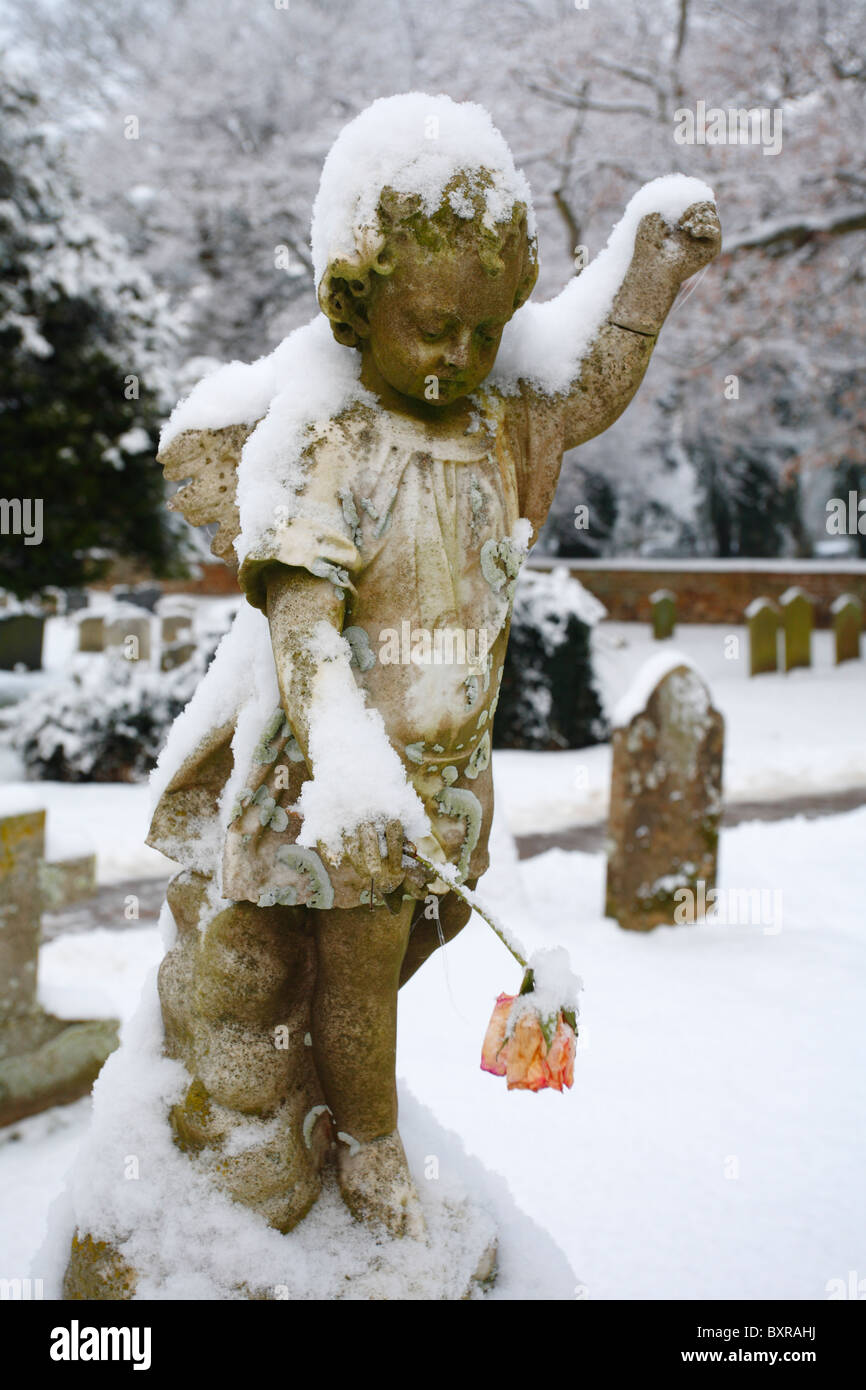 Bild von einem Cherub/Engel, die eine Blume im Schnee auf einem Friedhof bedeckt. Stockfoto
